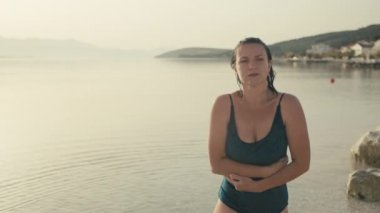 Girl comes out of the cold ocean water in a swimsuit. Beautiful young Caucasian woman after swimming in the sea go ashore. Beautiful and interesting vacation.
