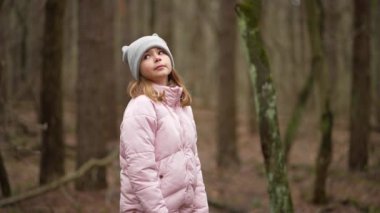 The girl in the gloomy forest looks in different directions. Mystical forest and one child looking at the tree without leaves in the spring. Slow motion 4K video of a natural landscape