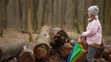The child opens a colorful umbrella in the rain. Girl walks in the park with trees in rainy weather. Slow motion 4K video of a landscape of a forest in which a man walks.
