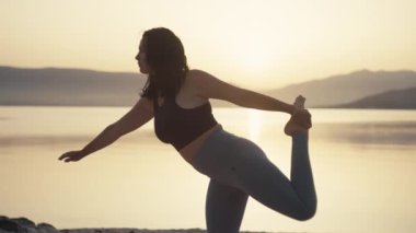 Güneş doğarken okyanusta sabah yogası. Spor kızı meditasyon yapıyor ve plajda spor yapıyor. Yüksek kalite 4k görüntü