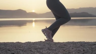 Slow motion video of female legs close up running on the beach at sunrise. A girl on a morning jog by the ocean is running around in sneakers. High quality 4k footage