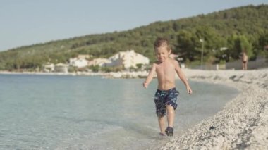 Deniz kenarında koşan bir çocuğun yavaş çekim videosu. Su damlaları ve çocuğun sevindiği güzel bir manzara..