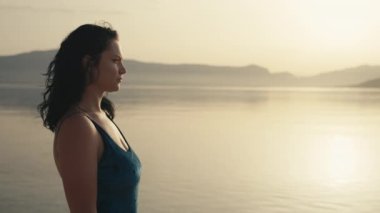 Denizde gün batımını izleyen bir kızın yakın çekimi. Mayo giymiş bir kadın, yazın okyanus kenarında dinlenir ve dinlenir. Yüksek kalite 4k görüntü