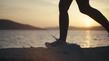 Spor ayakkabılı kadınların bacakları gün batımında okyanus kıyısında kayalıklarda koşar. Gün batımında koşan atletik bacakların yakın çekimi. Yavaş çekim videosu.