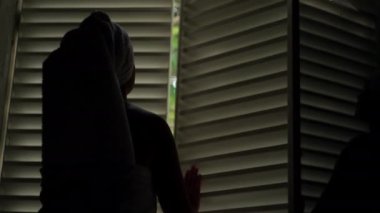 The Caucasian girl opens the window in the room from the morning. A woman wrapped in a towel after a shower opens the window in the apartment and lets in the suns rays. High quality 4k footage