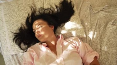 Caucasian girl wakes up and stretches in bed since morning. A woman opens her eyes when the sun hits her from the window. High quality 4k footage