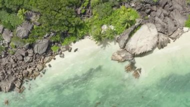 Aerial view of Seychelles. Coastline of a sandy beach near rocks and palm trees. Exotic vacation near the blue water of the Indian Ocean. High quality 4k footage