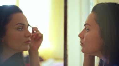 The girl does make-up at home near the mirror. A woman paints her eyebrows in an apartment interior. High quality 4k footage