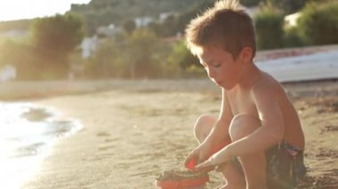 The boy plays in the sand on the beach. A child pours sand into a bucket and makes figures on a vacation near the ocean. High quality 4k footage