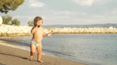 Little smiling girl running on the beach near the sea. A beautiful child on vacation is happy and takes his first steps. High quality 4k footage