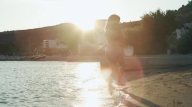 Slow motion video of a mother spinning her son on the beach by the sea. A happy and smiling family enjoys a vacation by the sea together. High quality 4k footage