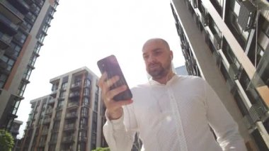 A businessman with a serious expression is walking and texting on the phone. The manager arranges business on a smartphone near the office. High quality 4k footage