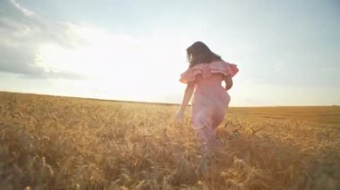 A beautiful woman in a dress walks through a wheat field and touches golden ears with her hands. The tenderness of a girl in nature and a sense of freedom. High quality 4k footage