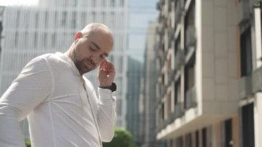 A businessman puts on headphones, turns on music and dances. A man smiles and rejoices against the background of a business center. Successful person. High quality 4k footage