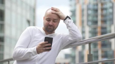 A male businessman in an urban landscape is texting on the phone and smiling. Positive emotion of a person in a cityscape. High quality 4k footage