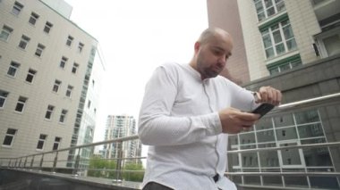 A businessman smokes an electronic cigarette and texts on the phone. The man is nervous and solves cases in the urban landscape. High quality 4k footage