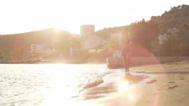 Slow motion video of a girl running on the ocean beach at sunset. A beautiful woman is happy touching the water with her feet and the waves splashing in the water. High quality 4k footage