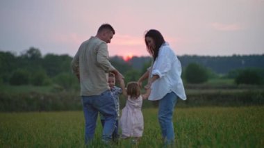 Family holding hands dancing at sunset in nature. Happy parents and children rejoice and have fun together. High quality 4k footage