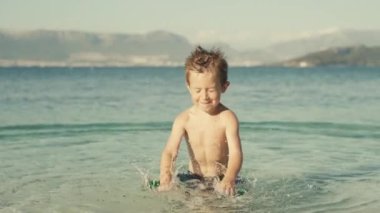 Slow motion video of a cheerful boy swimming and splashing water in the ocean. The child is playing in the sea on vacation smiling and happy.