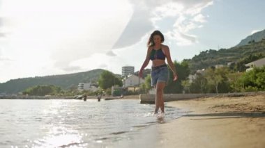The girl is walking along the ocean shore, splashing the water with her feet. A Caucasian woman walks along the seashore. slow motion video. High quality 4k footage