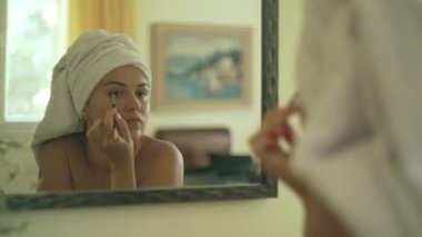 Caucasian woman doing eye make-up in front of the mirror. A Girl in a towel paints her face before a party. A woman is preparing to be afraid. High quality 4k footage