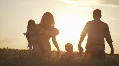 A happy family is walking through a wheat field at sunset. A farmer and his family inspect the fields and teach children to work together in a beautiful natural landscape. High quality 4k footage