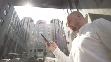 A businessman uses a phone at work near a business center. A serious man is texting on a smartphone, signing contracts. High quality 4k footage