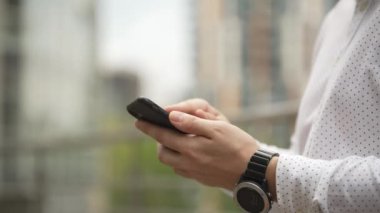 Close-up of a man texting on the phone with positive emotions. A businessman in a cityscape shakes his head approvingly because he has succeeded in everything. High quality 4k footage