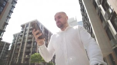 A businessman walks and communicates on the phone, solving cases. A serious man walks near a business center and writes a message on a smartphone. High quality 4k footage