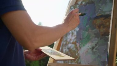 A male artist dips a brush in paint and paints an abstract picture in nature. Hobbies and relaxation alone in the field at sunset. High quality 4k footage