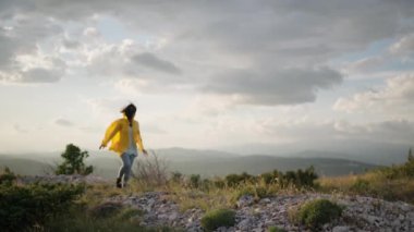The girl is trekking in the mountains. A woman in a yellow jacket walks along a mountain range in a beautiful landscape on a hiking trip. High quality 4k footage