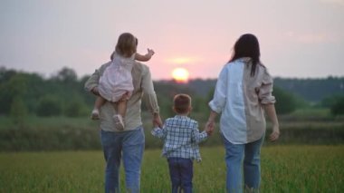 A happy family walks in the park holding hands. childrens and adult dreams. Fanny walk together. Smiling and cheerful at sunset in a field in nature. High quality 4k footage
