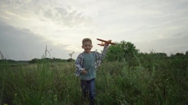A boy runs on the grass with an airplane in his hands. A child flies in his dreams. Active games in nature. Happy and smiling boy. Slow motion video. High quality 4k footage