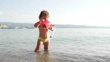 A child plays with toys in the sea. A happy girl on vacation is playing with ocean water, overflowing the water. High quality 4k footage