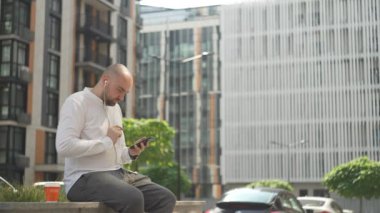 A man listens to music and dances while drinking coffee. Businessman in casual clothes on lunch break. High quality 4k footage