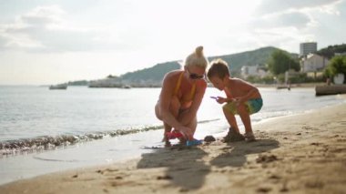 Mother and son are sculpting pyramids on the beach by the sea. Family summer vacation together. High quality 4k footage