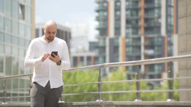 Günlük giysiler giymiş bir adam şehir manzarasında telefonla mesajlaşıyor. Aletle ilgili yazışmalardan sonra adam mutsuz oldu. Yüksek kalite 4k görüntü
