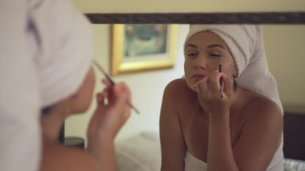 欧洲女孩在镜子旁边画她的眼睛 披着毛巾的女人在家里化妆 一个漂亮的女孩正在准备参加一个去餐馆的聚会 高质量的4K镜头 — 图库视频影像