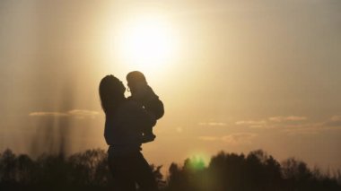 Bir annenin kızının kollarını sarmaladığı yavaş çekim videosu. Aile konsepti mutluluğu sever. Bir aile gün batımında doğada birlikte vakit geçirir.