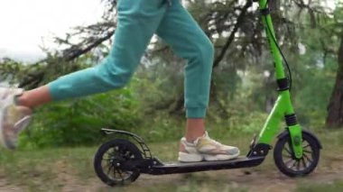 Scooter kullanan bir kızın bacaklarının yakın çekimi. Mutlu aile parkta yürüyor. Ayakların yerden kalktığını gösteren yavaş çekim videosu. Yüksek kalite 4k görüntü