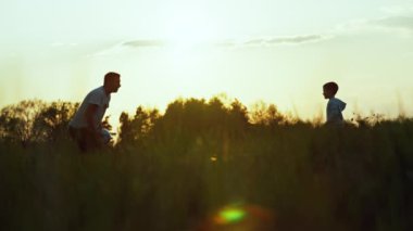 Yavaş çekim video siluetleri baba ve oğulun top oynarken. Bir adam çocuğuna dışarıda futbol oynamayı öğretiyor. Parkta mutlu bir aile. Yüksek kalite 4k görüntü