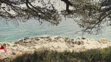 Çantalı bir kız deniz kenarındaki kayalıklarda güneşlenmeye gider. Okyanus kenarında tatilde olan güzel bir kadın. Yüksek kalite 4k görüntü