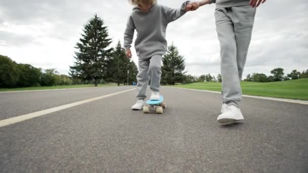 妹は公園でスケートをするように弟に教える 友達の助けの少年は 一緒に過ごした時間 スケートに乗って足のクローズアップ 高品質4K映像 — ストック動画