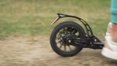Scooter kullanan bir kızın bacaklarının yakın çekimi. Mutlu bir çocukluk ve parkta yürüyüş. Yavaş çekim videosu. Yüksek kalite 4k görüntü