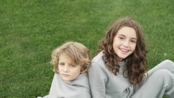 兄と妹が草の上に座って一緒に笑っている 家庭を取るという概念です 高品質4K映像 — ストック動画