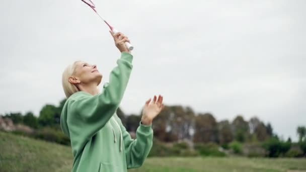 公園でバドミントンをしている先輩女性のスローモーションビデオ 幸せな笑顔の人が積極的に時間を費やしています ラケットを持ってテニスをしている女性 高品質4K映像 — ストック動画