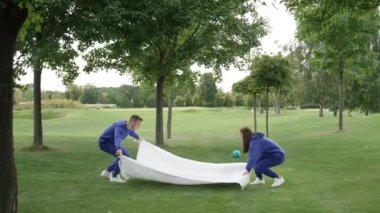 Ebeveynler parkta piknik yapmak için battaniyeyi açar. Aile eğleniyor ve birlikte vakit geçirmekten zevk alıyor. Yaşam tarzı video neşesi aile mutluluğunu gülümsetir. Yüksek kalite 4k görüntü