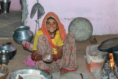 Büyükanne, eski bir mutfağın kırsal bir köyünde toprak chulhas 'ta yakacak odun kullanarak taze yemek yapıyor ve pişiriyor. Gülümse..