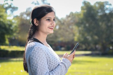 Açık havada gülümseyen bir kızın cep telefonu kullanması ve yan bakması..