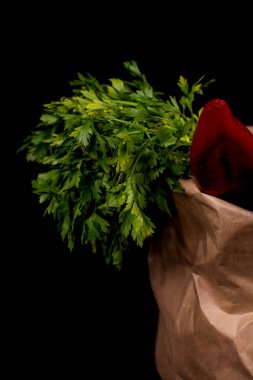 Taze sebzeli kağıt poşet. Pırasa, kırmızı dolma biber, maydanoz siyah arka planda bir kese kağıdında yatıyor..